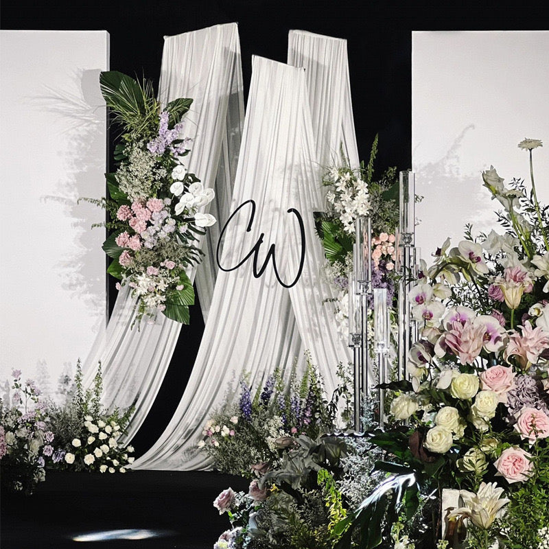 Elegant drapery arch stand with white fabric and floral decorations set up outdoors for a wedding ceremony.