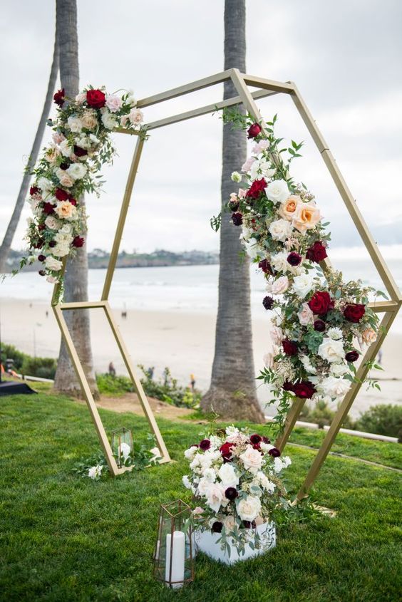 Double-layer gold metal hexagon arch with greenery and flowers for an outdoor event.