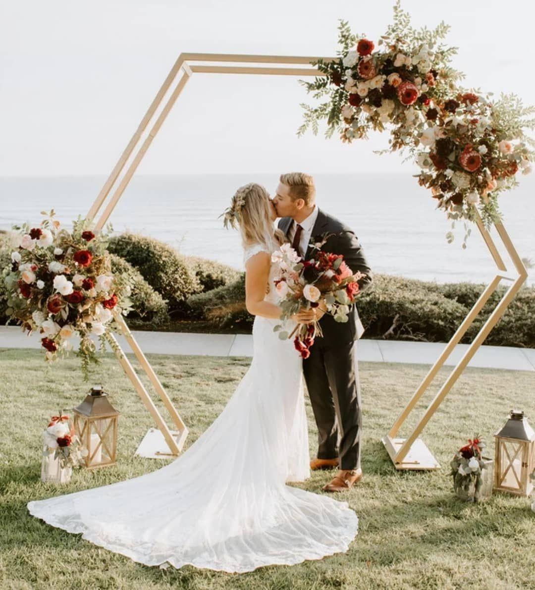 Elegant double-layer gold metal hexagon arch with floral decorations for a wedding.