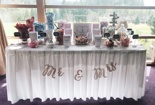 Candy Bar Set with glass terrariums, satin linen, and silver bejeweled scoops displayed at an event.
