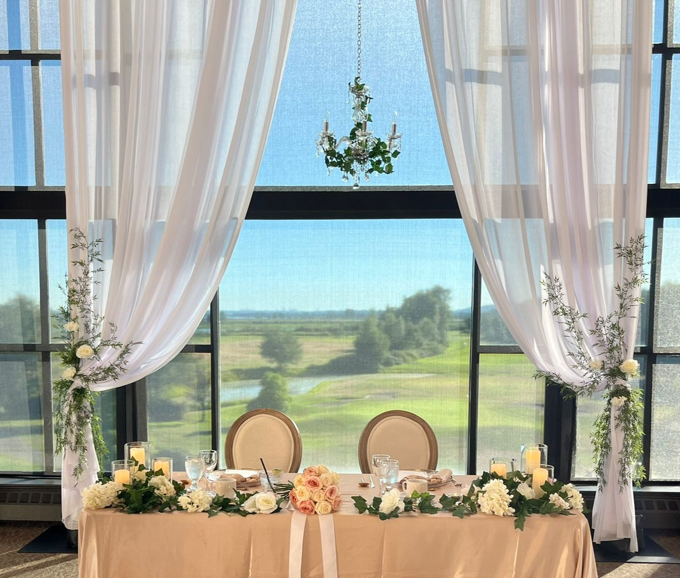 Silk faux greenery and floral on white drapes creating an elegant backdrop for an event.