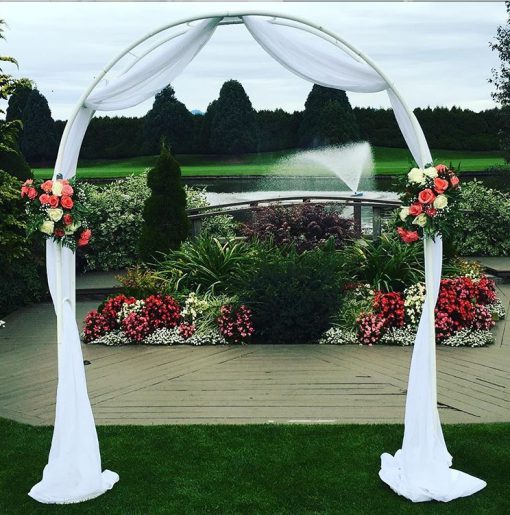 Elegant white metal arch used as a backdrop for an outdoor garden event.