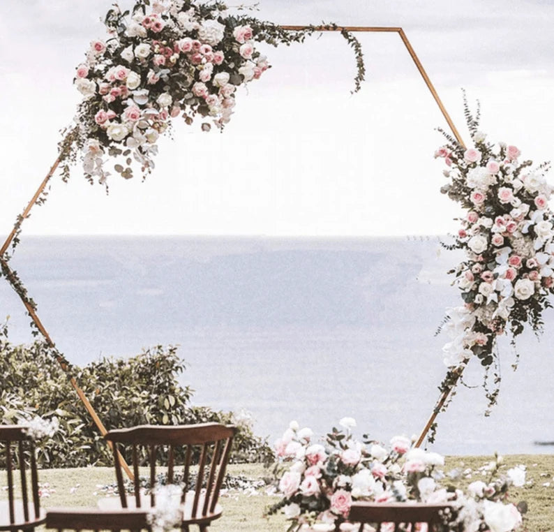 Stunning gold metal hexagon arch decorated with flowers for a wedding by the seaside.