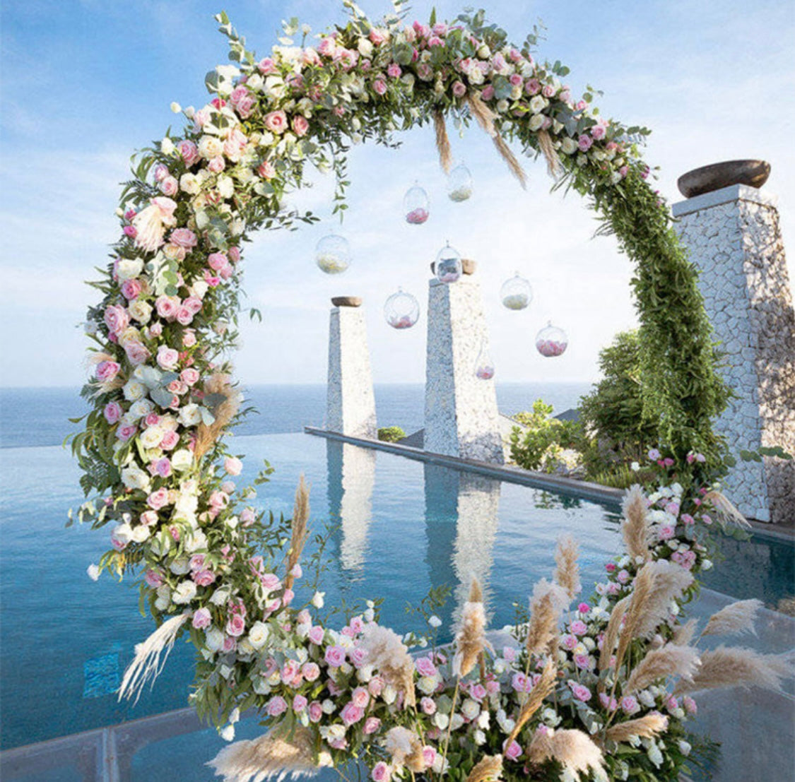Round Metal Arch adorned with pink and white flowers, set against a scenic backdrop by the sea