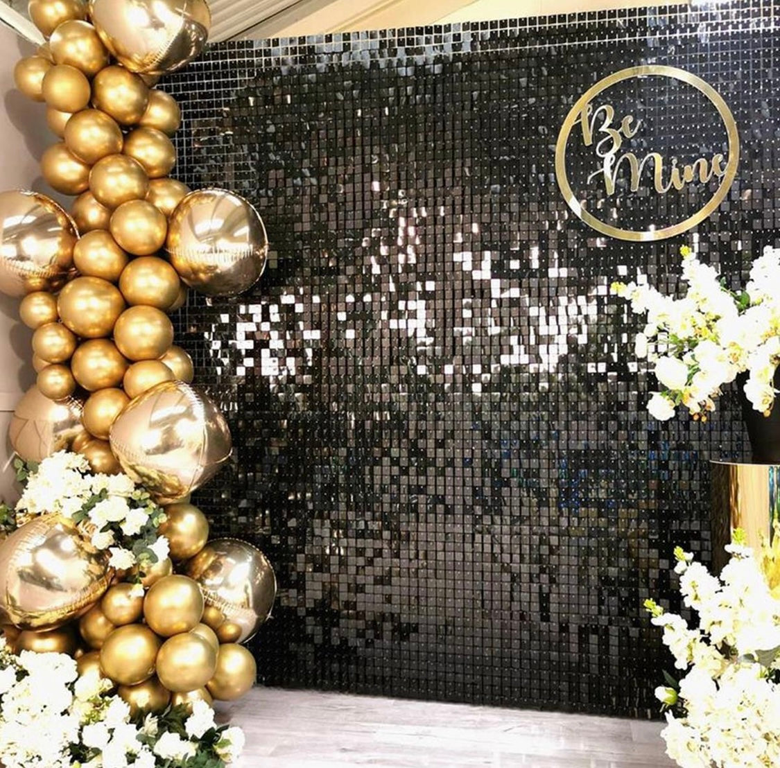Black sequin shimmer wall backdrop decorated with gold balloons and flowers.