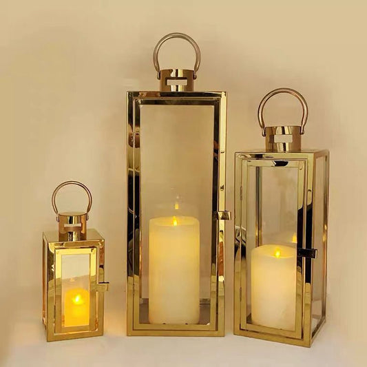 Set of three gold and glass lanterns with lit candles inside.