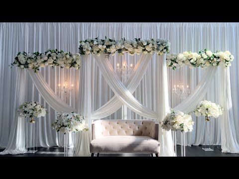 Elegant white draping backdrop with floral arrangements for a wedding.