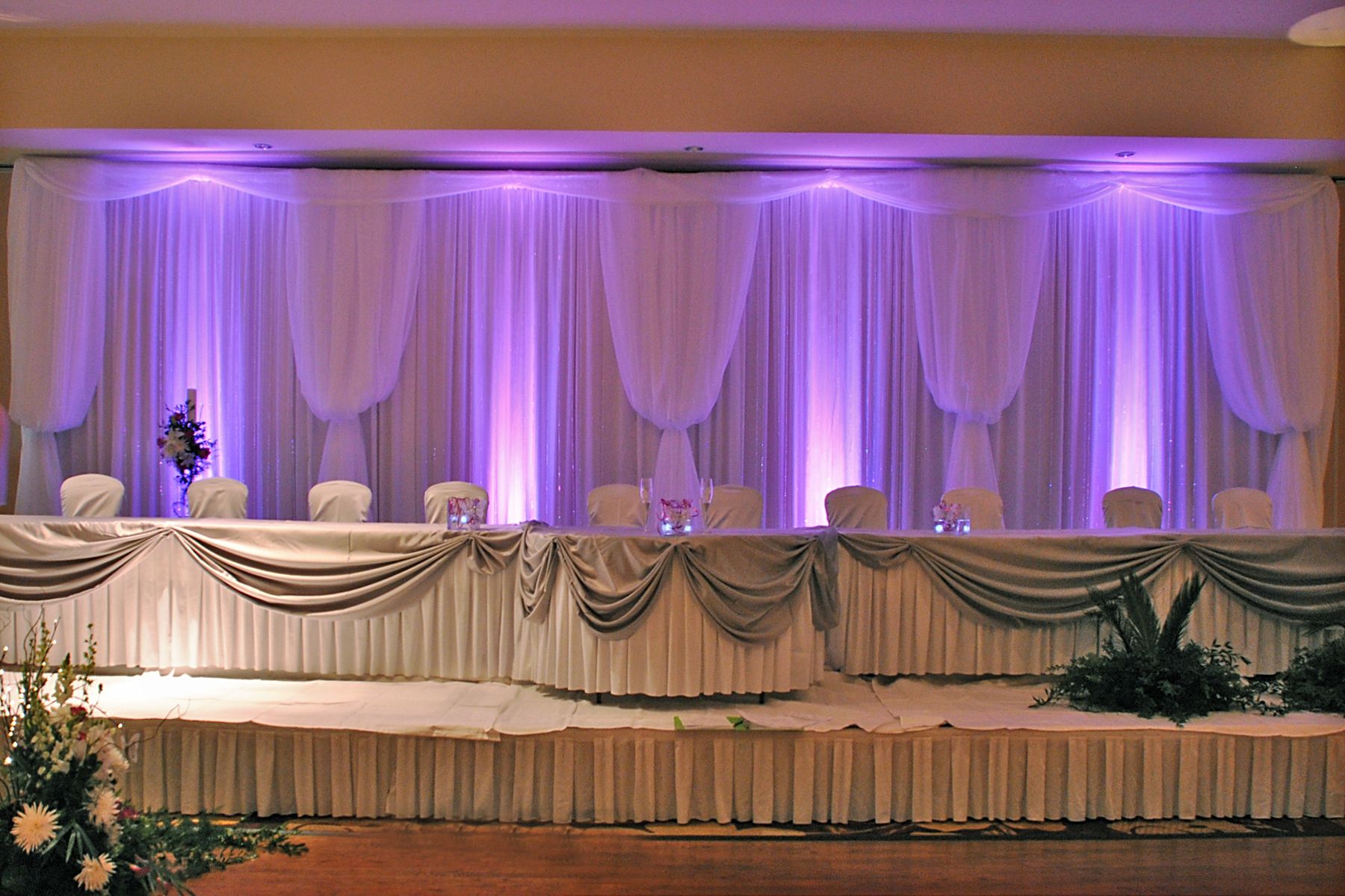 Backdrop with purple draping and uplighting for a wedding reception.