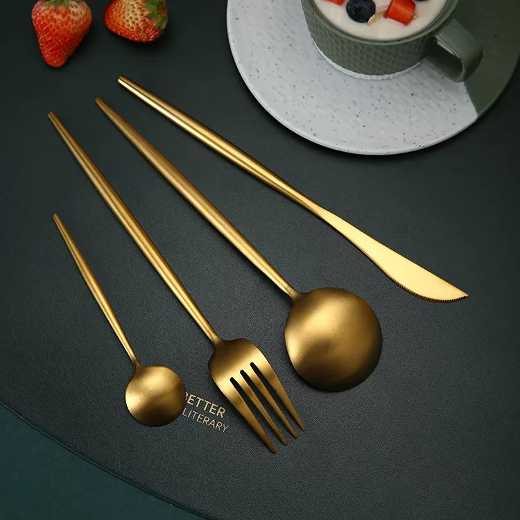 Gold matt stainless steel cutlery set arranged on a dark green tablecloth.